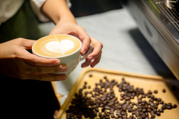 Barista who prepares coffee drinking is pouring milk foam to heart shape into  the cup to make coffee latte art. image for background, wallpaper, decoration, interior and copy space.