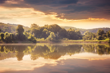 Naklejka na ściany i meble River and forest at sunset. Display trees and clouds in the water of the lake. Landscape with a river and trees in the evening_