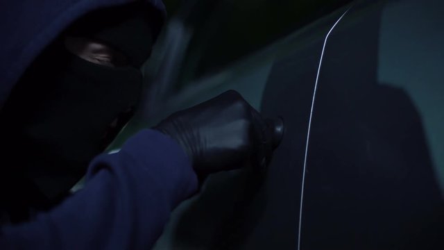 Male robber unlocking car at night with tool, young lawbreaker at parking place