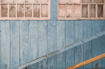 Pale blue wooden wall of village house with windows and handrails. The windows reflect the sunset