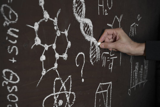 A man's hand from darkness writes  DNA code and formulas on an improvised chalkboard.  Shallow depth of field
