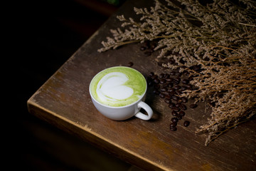 Focused green tea cup on wood table with coffee beans and spike on background.  daily aroma drinking concept. latte art image for decoration, interior design background, wallpaper and copy space.