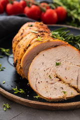 Stuffed turkey breast with baked vegetables and spices on a black background.