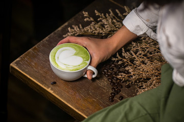 Focus green tea latte art on the wood table which hold on by barista's hand. latte art image for decoration, interior design background, wallpaper and copy space. latte lover concept.