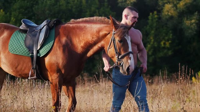 A young man weightlifter walking on the field, next to him is a beautiful horse