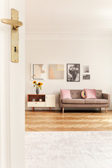 Pink cushions on beige sofa next to white cabinet with sunflowers in spacious interior with posters. Real photo