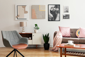 Grey armchair in living room interior with lamp and plant on cabinet next to beige sofa. Real photo