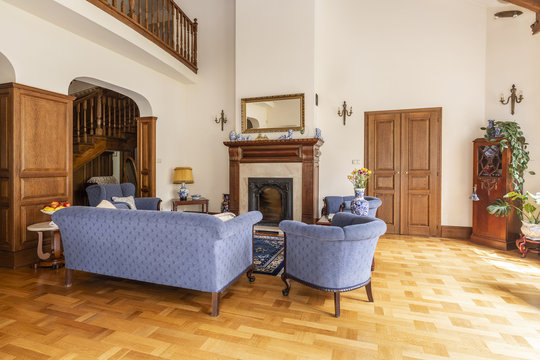 Real photo of a blue set of sofa and chairs in an elegant living room interior with wooden furniture and classic fireplace