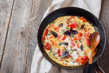 Omelet with vegetables in a pan close-up. Wooden background, top view horizontal. Copy space