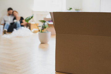 Close-up on carton box on the floor during packaging. Plant and couple in the background