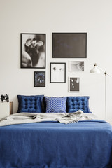 Patterned pillows on bed in navy blue and white bedroom interior with lamp and posters. Real photo
