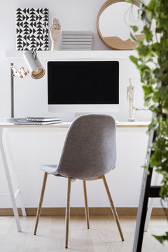 Grey chair at desk with lamp and desktop computer in simple white workspace interior. Real photo