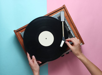 Female hands  use retro vinyl player on a blue pink pastel background. DJ. Top View.