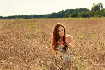 A young girl with red hair carefully reviews the ears of wheat on a rural field