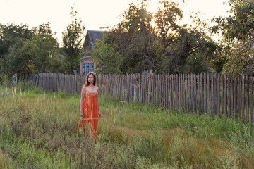 frightened lonely retro girl in the countryside walking along the high grass in the evening along...