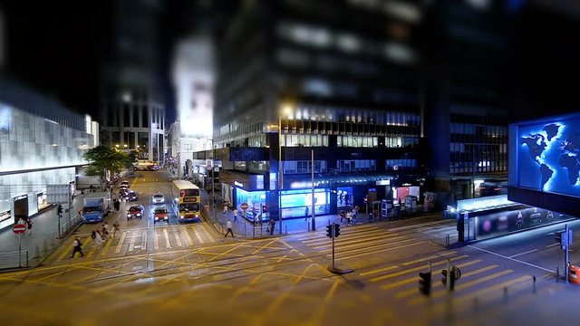 Hectic city nightlife. Taxi cabs, double deck buses, trams crossing a crossroad in the central district. People fast walking pedestrian crossing. Time lapse with tilt-shift effect