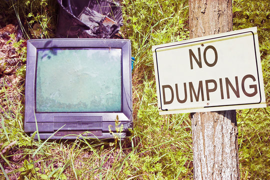 Old television CRT (Cathode ray tube) abandoned in nature with "No Dumping" text - concept image with copy space
