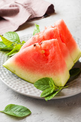 Watermelon sliced on a plate with mint leaves on a wooden background.