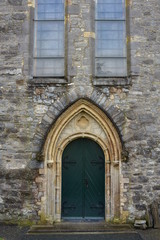 Arched dual door on metal hinges on side wall of stone medieval cathedral.