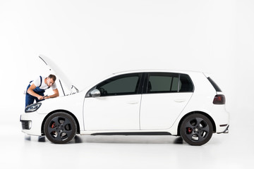 handsome auto mechanic repairing car and looking in open hood on white