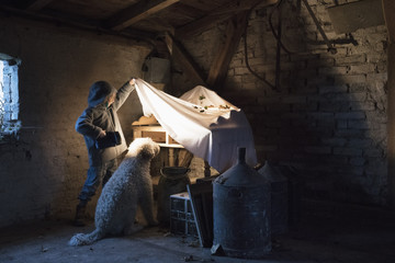 Girl and dog with flashlight peeking under cloth in carpentry workshop
