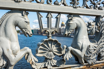 Metal bridge with a forge with forged patterns of horses and tridents in the background Isaak's Cathedral.