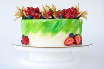 Cake with whipped green cream, decorated with fresh strawberries, blueberries, figs and physalis on white background. Picture for a menu or a confectionery catalog.