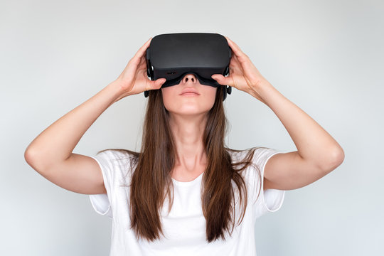 Young woman wearing virtual reality goggles headset, vr box. Connection, technology, new generation, progress concept. Girl trying to touch objects in virtual reality. Studio shot on gray