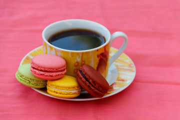 Cup of coffee with tasty colorful macarons on pink background