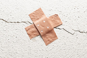 band-aid plaster in cross shape on a crack in the wall, concept for botched construction and...