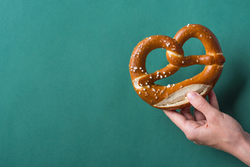 Young woman hold in hand German savory lye pretzel with salt on dark green background. Poster Banner for Bakery Coffee Shop Menu. Oktoberfest Card. Copy Space - obrazy, fototapety, plakaty