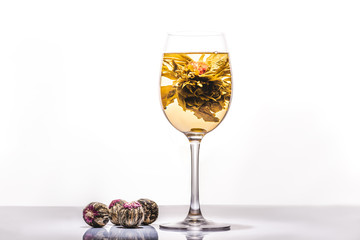 glass of tasty chinese flowering tea with tea balls on reflecting table