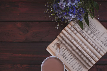 Beautiful bouquet of cornflowers, book, coffee and feather on the wooden table.