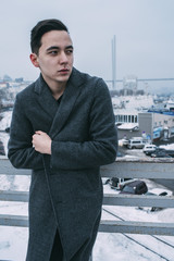 Young man in long coat on urban winter bridge