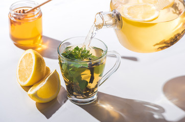 pouring healthy tea with lemon and mint from teapot into cup on white tabletop