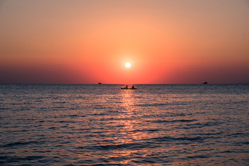 Rowing boat at the sea with orange sun setting over the horizon