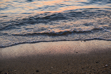 Edge of the beach close up with small water ripples reflecting the sunset colors