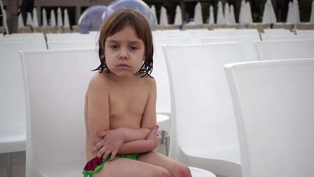 Portrait of a child who is cold. Girl 4-5 years after swimming in the pool. A child is sitting on a white chair. Many chairs are places for spectators or sports fans. Shooting close-up.