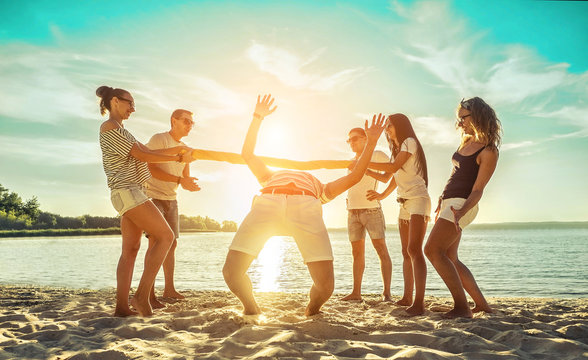 Happiness young funny girls and guys Friends funny game on the beach under sunset sunlight
