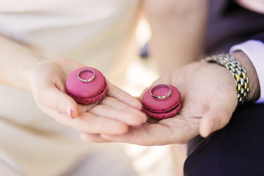 Wedding couple holding macaroons with the rings. Wedding theme.