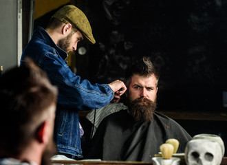 Hipster client getting haircut. Barber with hair clipper works on hairstyle for man with beard,...