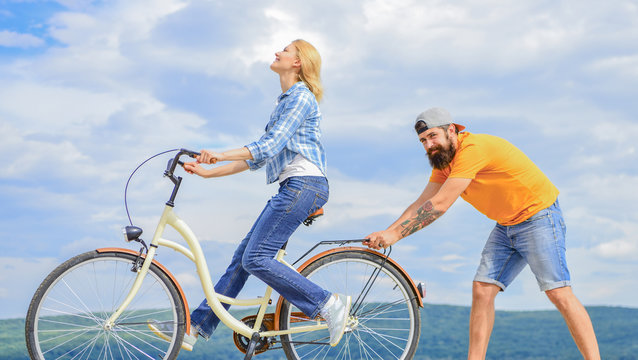 Girl Cycling While Boyfriend Support Her. Teach Adult To Ride Bike. Man Helps Keep Balance And Ride Bike. Find Balance. Woman Rides Bicycle Sky Background. How To Learn To Ride Bike As An Adult