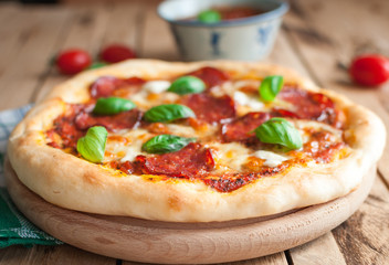 Close-up of homemade rustic pizza with salami, mozzarella and fresh basil on top