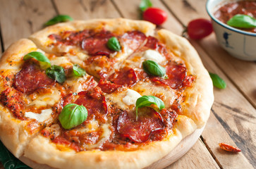 Close-up of homemade rustic pizza with salami, mozzarella and fresh basil on top