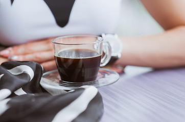 Woman's hands with a cup of coffee and black and white scarf in the cafe