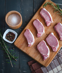 Raw pork chops on cutting board with seasonings, top view