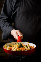 Cropped view of chef cooking Italian pasta with cheese, vegetables and egg yolk on hot pan flying.