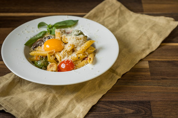 Italian pasta with cheese, vegetables and egg yolk served portion on wooden background.