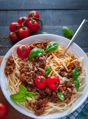 Close-up of Italian spaghetti with tomato sauce, Parmesan cheese and fresh basil on top, on dark background