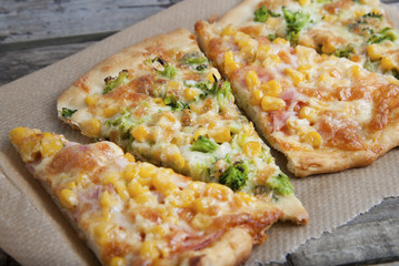 Mix slices of homemade pizza with cheese, sweet corn, bacon and spinach leaves, on wooden background